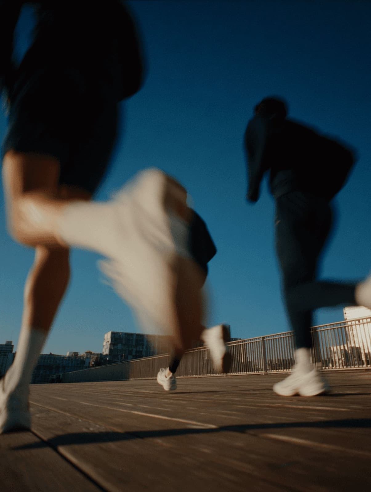Three athletes accelerating across a boardwalk under a deep blue sky