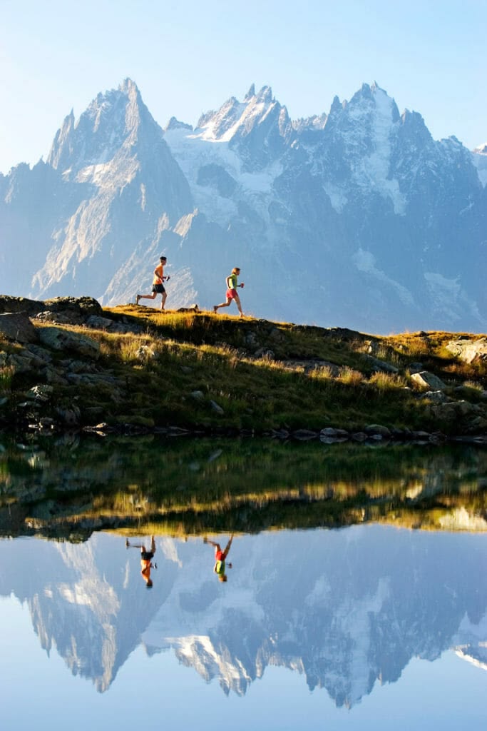 Two runners on a ridge above Chamonix, the aiguilles rising behind them.